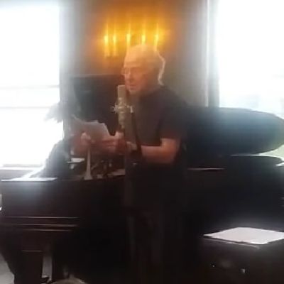 Tom Paul is performing as he is reading the pages he is holding.